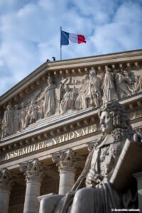 Vue de la façade et des colonnades de l’Assemblée nationale française, avec le drapeau tricolore flottant au sommet.