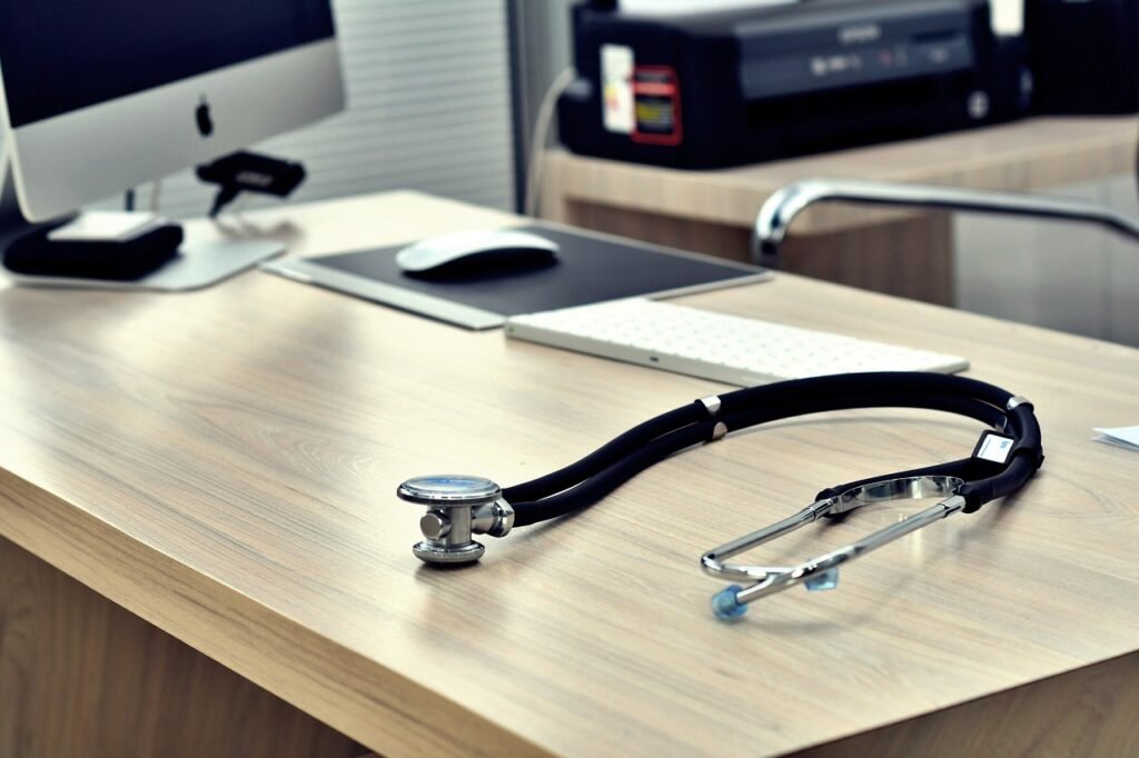 Stéthoscope posé sur un bureau médical avec un ordinateur et une imprimante en arrière-plan.
